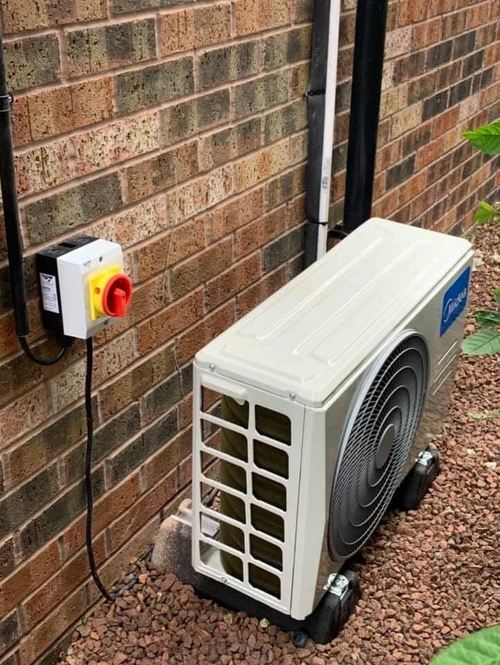 Air conditioning condenser on a gravel base with its isolator switch alongside