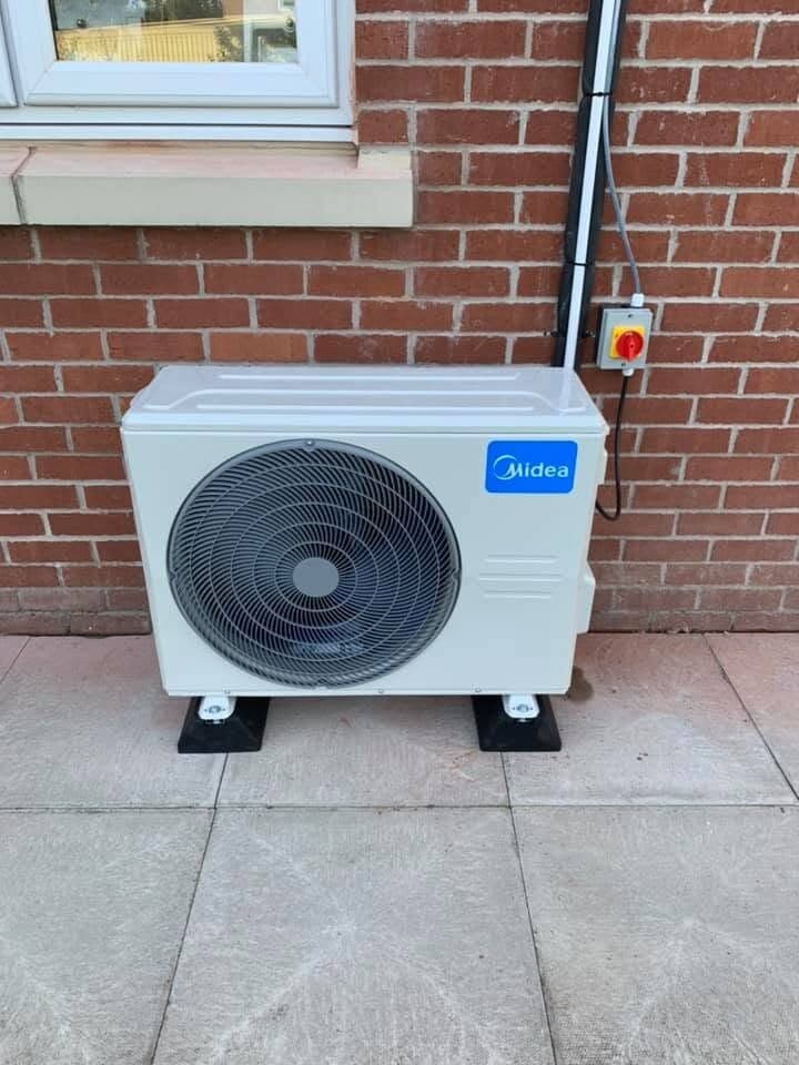 Air conditioning condenser stood on paving beside a brick house wall