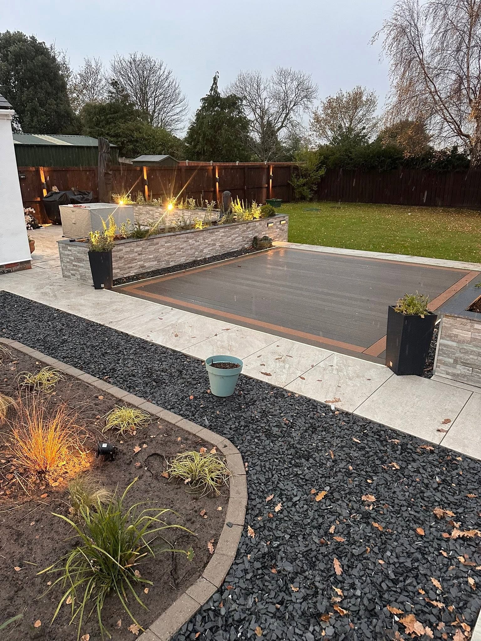 Deck, lit planters and gravel bed running down to the lawn in the evening