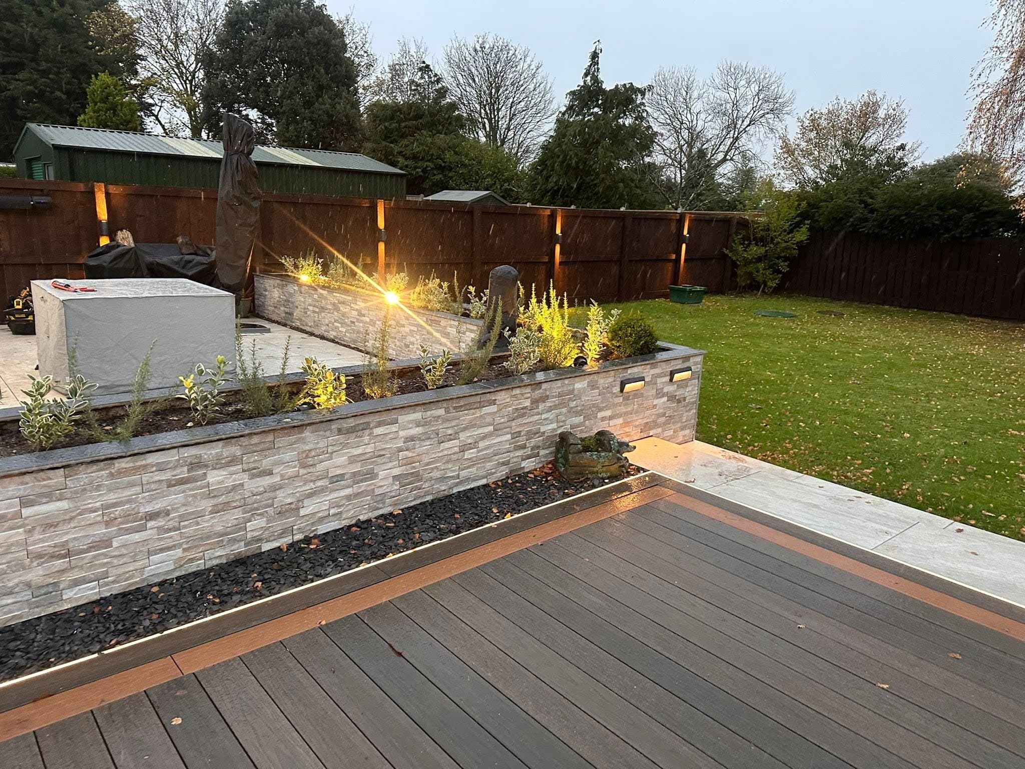 Composite decking with recessed brick lights set into the retaining wall and uplights along the fence line