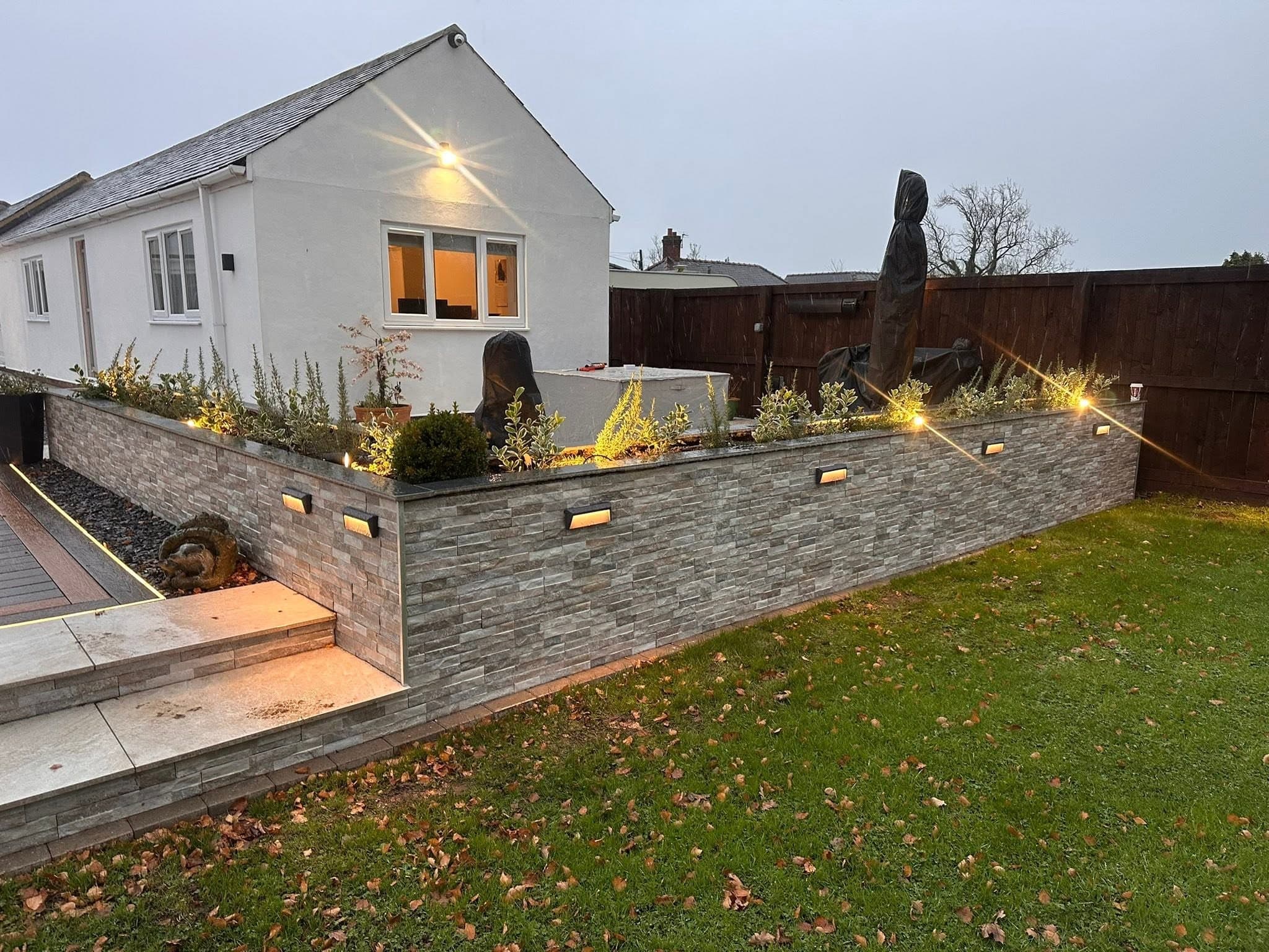 Rendered gable end floodlit at dusk with recessed lighting to the stone-clad wall below