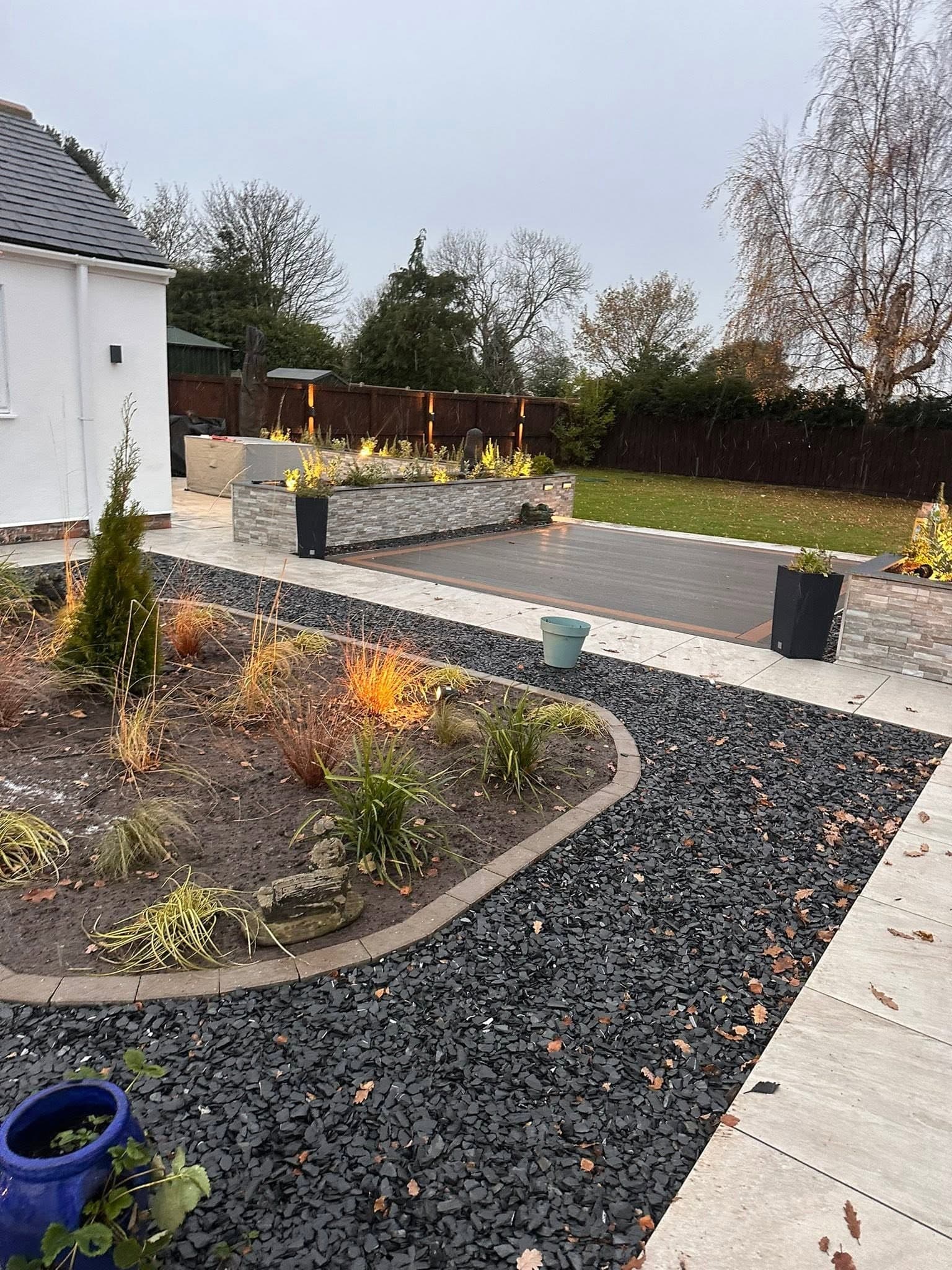 Planted beds and slate chippings lit by spike spotlights beside composite decking