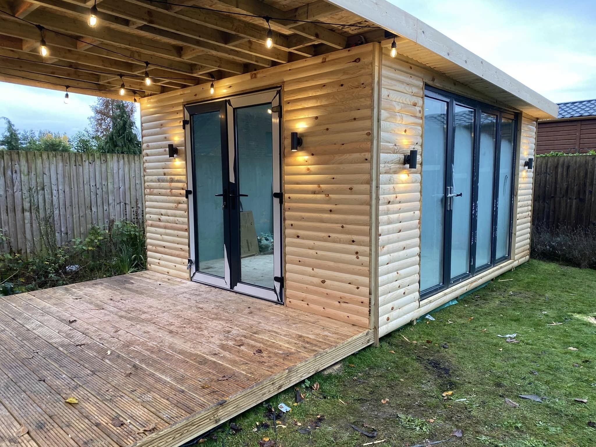Timber-clad garden room with wall lights and a composite deck at dusk