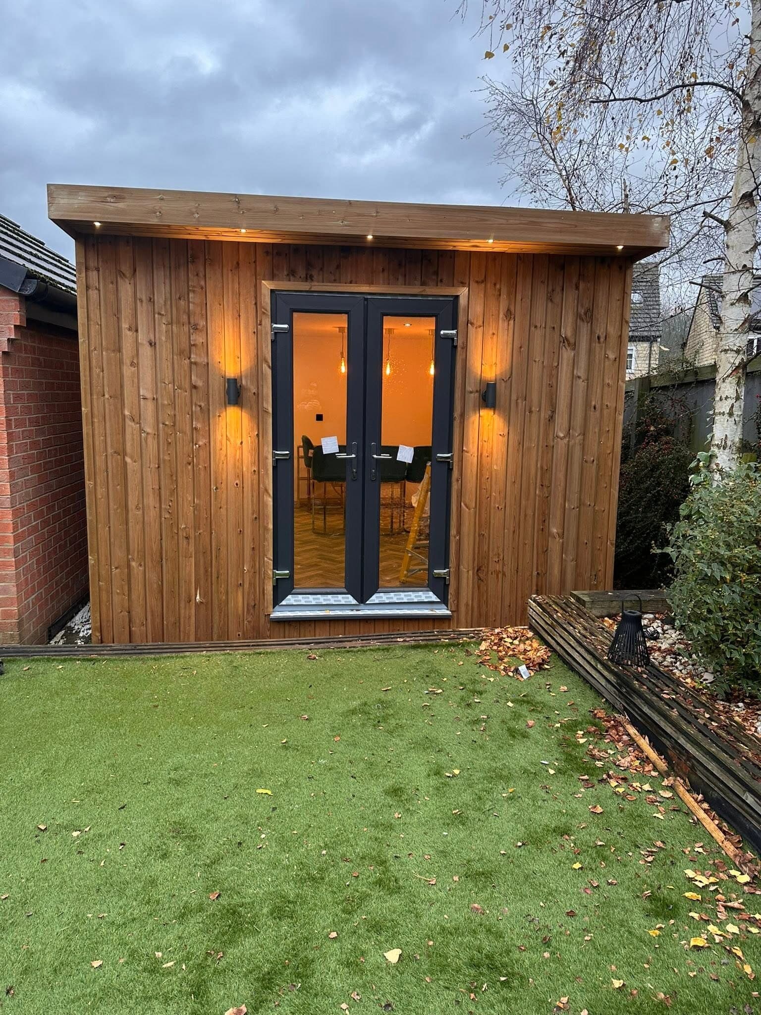 Garden office exterior at night with warm wall lights either side of the doors