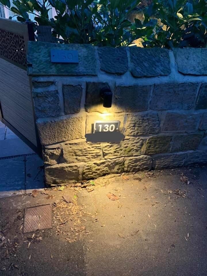 Illuminated house number set into a stone garden wall