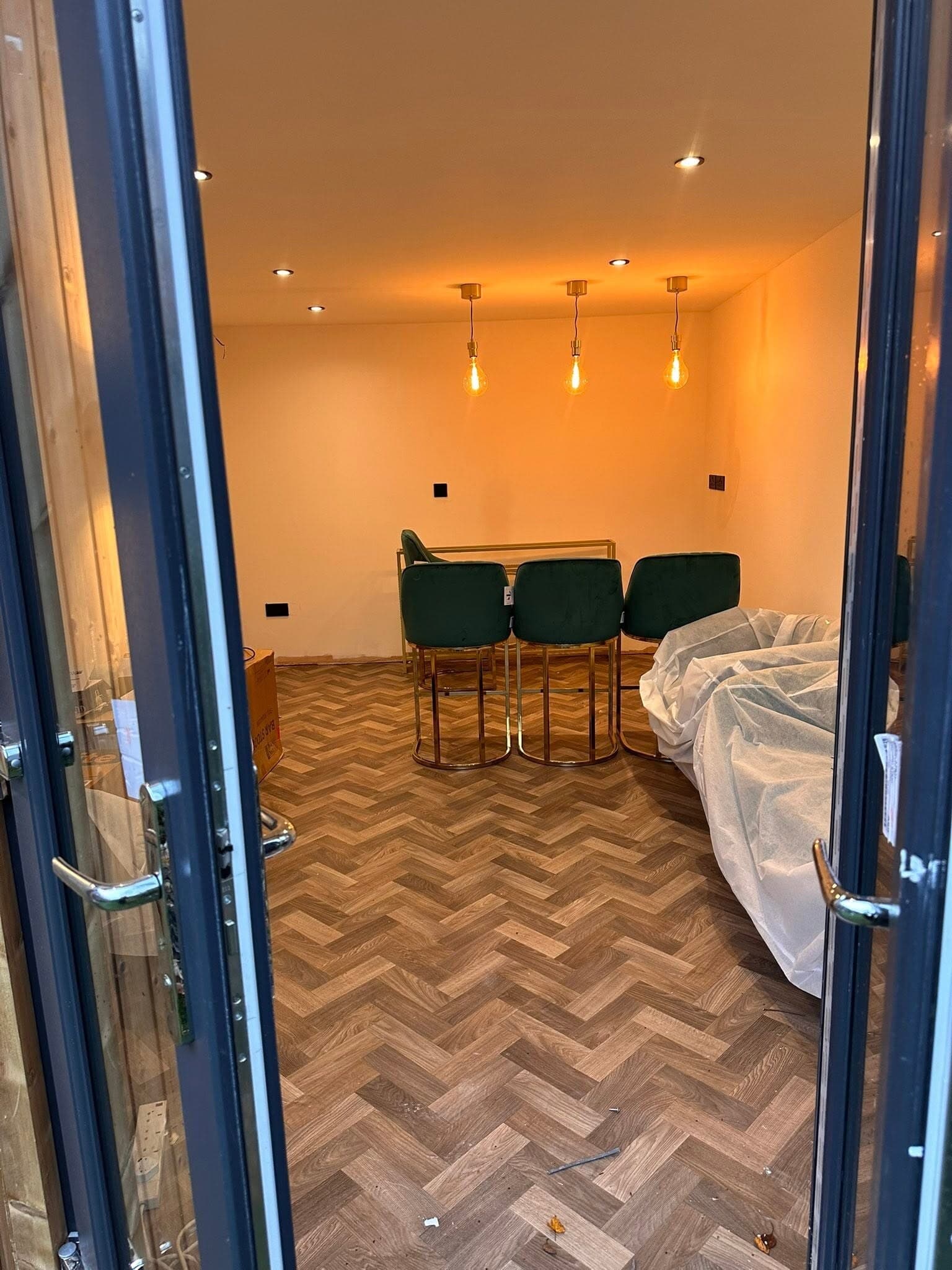 Herringbone-floored room lit by a row of warm pendant lights