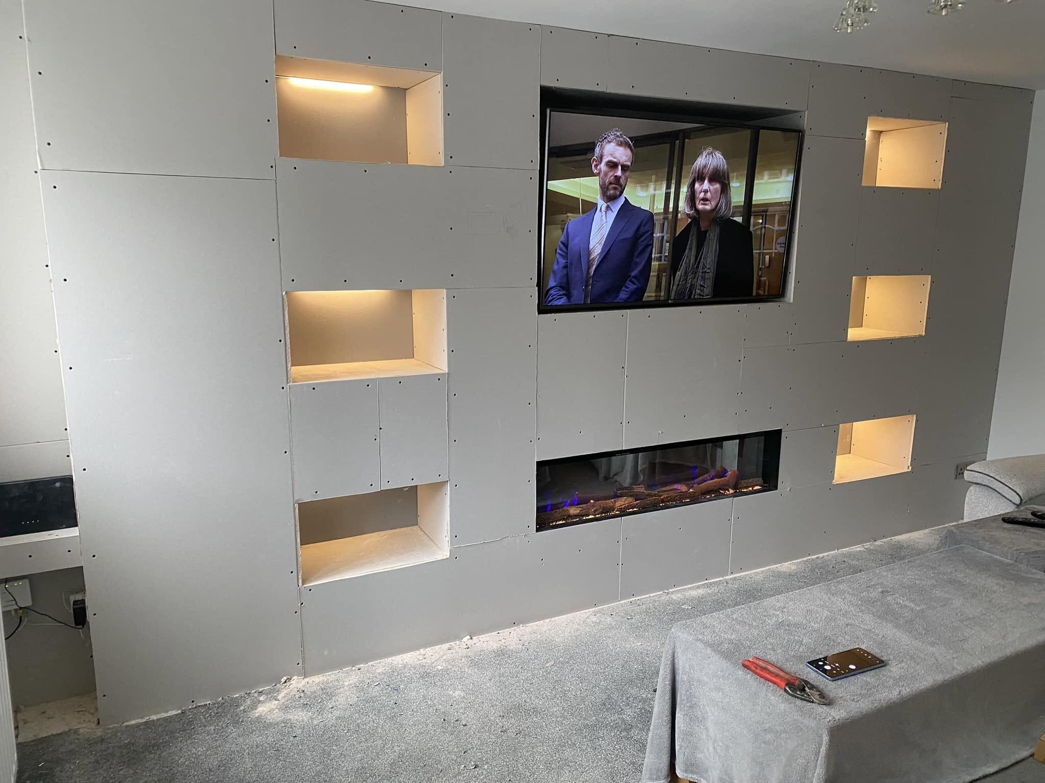 Media wall with warmly lit recessed niches either side of the television and fire