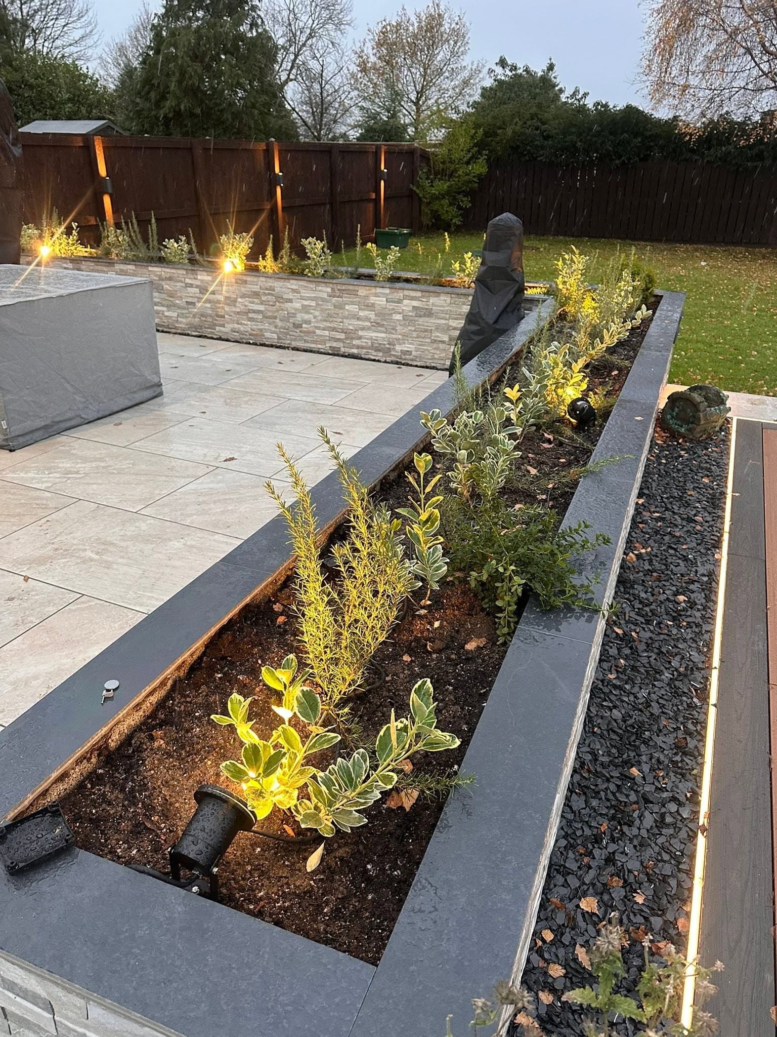 Twin raised planters lit from within with fence uplights and lawn beyond