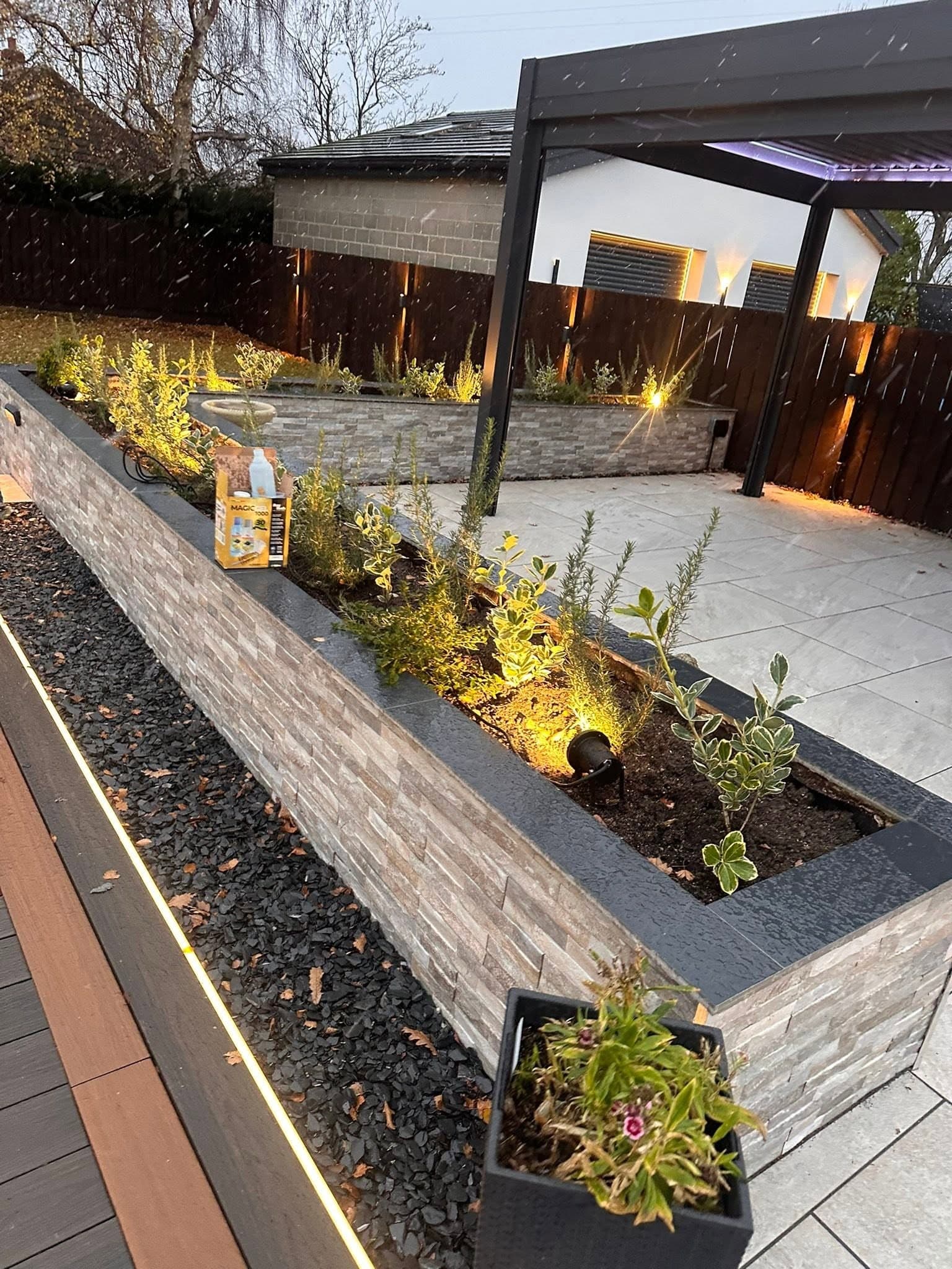 Stone-clad raised planter lit by spike spotlights with deck-edge LED strip behind