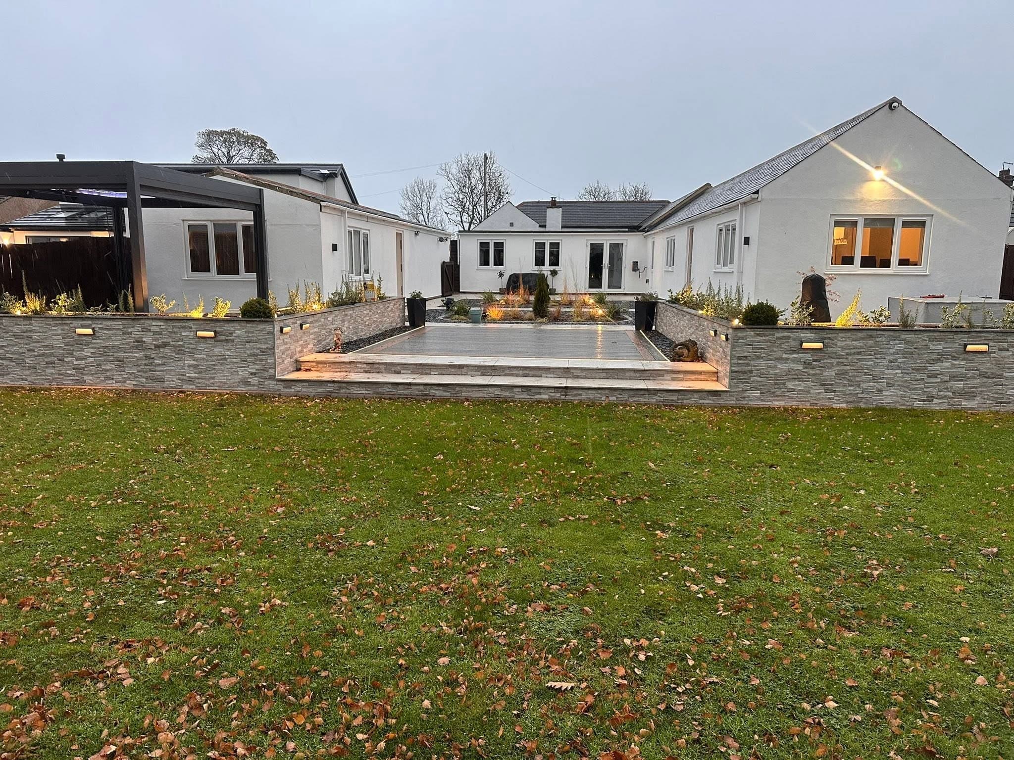 Whole rear elevation of a rendered bungalow at dusk with the full garden lighting scheme lit
